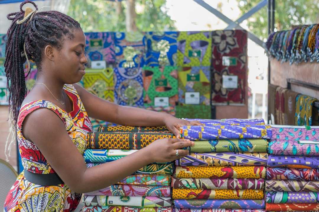 A trader arranging colourful fabric in a market stall; illustrative stock photograph by Iwaria Inc. / Unsplash.